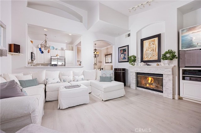 living area with light wood-style flooring, track lighting, arched walkways, and a glass covered fireplace