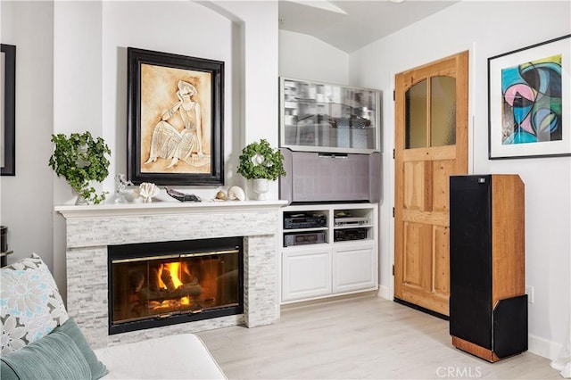 sitting room with light wood finished floors, a stone fireplace, vaulted ceiling, and baseboards