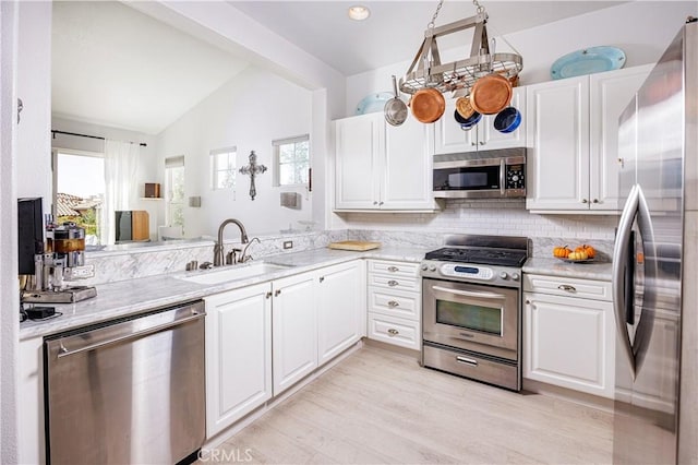 kitchen featuring stainless steel appliances, a sink, vaulted ceiling, light countertops, and white cabinets