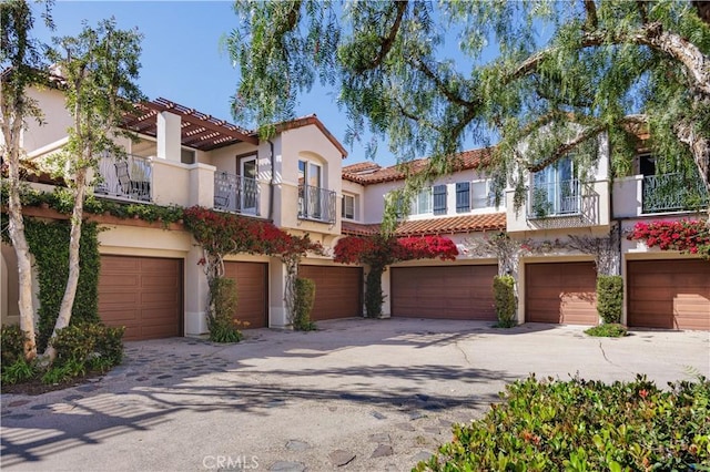 view of front of house with an attached garage, a tile roof, stucco siding, driveway, and a balcony