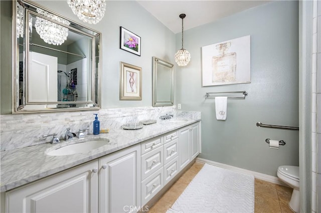 bathroom with a chandelier, double vanity, toilet, tile patterned flooring, and baseboards