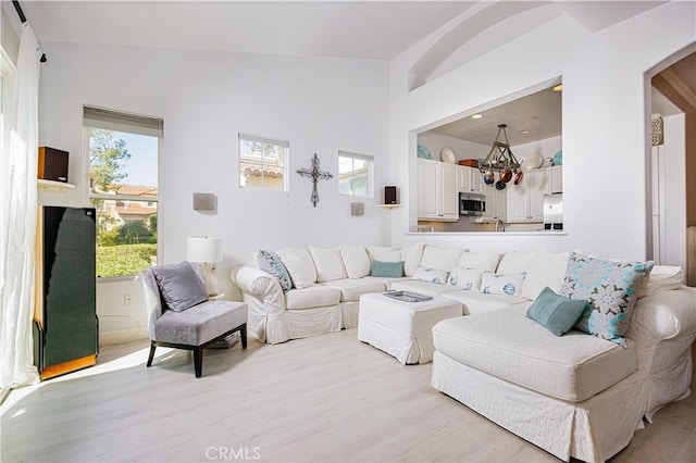 living area featuring light wood-style floors, arched walkways, a chandelier, and lofted ceiling