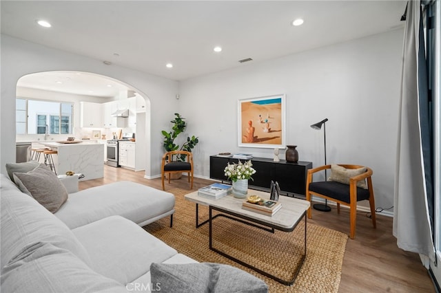 living area with arched walkways, recessed lighting, light wood-style floors, and baseboards