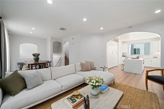 living room featuring arched walkways, light wood finished floors, recessed lighting, and stairway