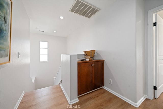 hallway with an upstairs landing, wood finished floors, baseboards, and recessed lighting