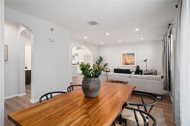 dining room featuring wood finished floors, arched walkways, recessed lighting, and baseboards