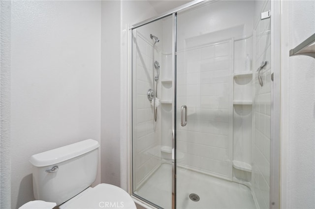 full bathroom featuring a stall shower, toilet, and a textured wall