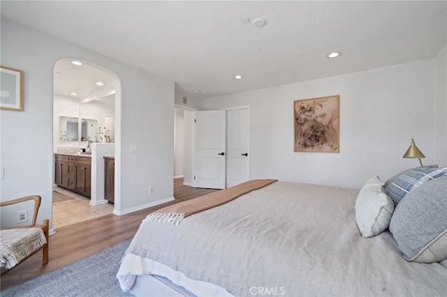 bedroom featuring recessed lighting, light wood-style flooring, arched walkways, and ensuite bathroom