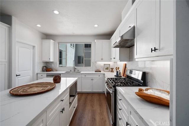 kitchen with stainless steel gas range, under cabinet range hood, tasteful backsplash, a sink, and white cabinets