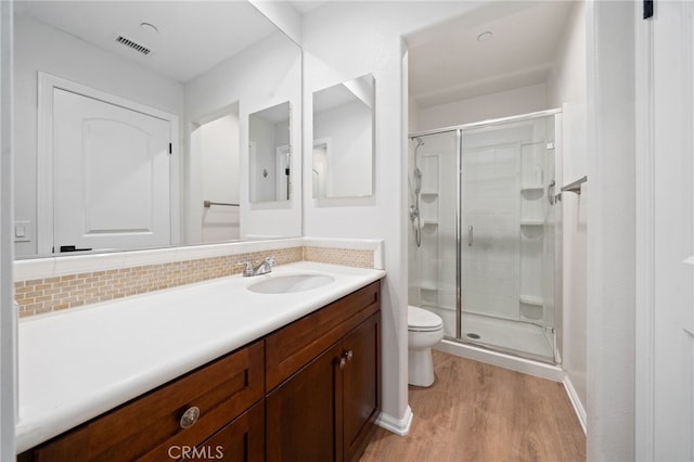 bathroom featuring toilet, wood finished floors, a shower stall, vanity, and tasteful backsplash