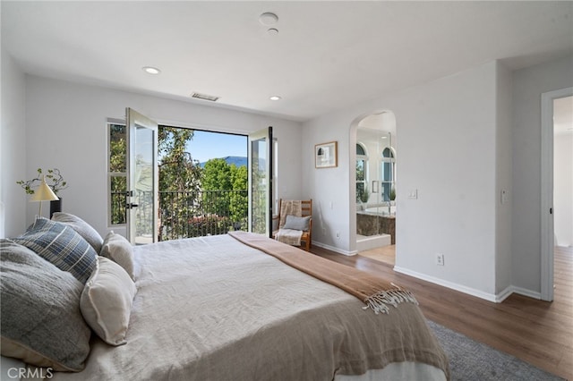 bedroom with arched walkways, wood finished floors, baseboards, recessed lighting, and ensuite bathroom