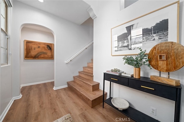 stairway with wood finished floors, baseboards, recessed lighting, and arched walkways
