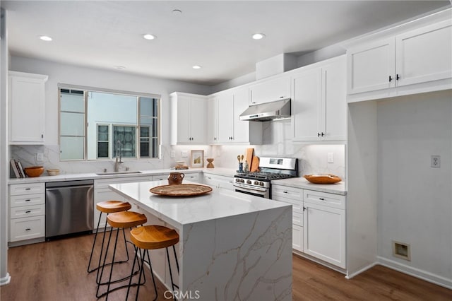 kitchen with appliances with stainless steel finishes, under cabinet range hood, dark wood-type flooring, white cabinetry, and a kitchen island