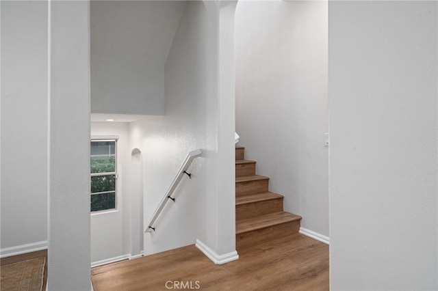 staircase with wood finished floors, arched walkways, and baseboards
