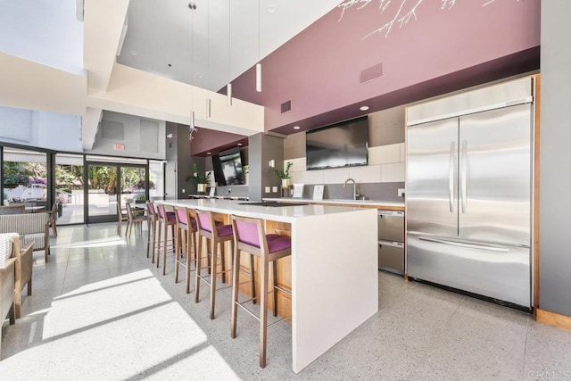 kitchen featuring built in fridge, a towering ceiling, dark aggregate flooring, light countertops, and modern cabinets