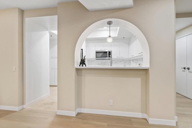 kitchen featuring stainless steel microwave, light wood-style floors, baseboards, and white cabinets