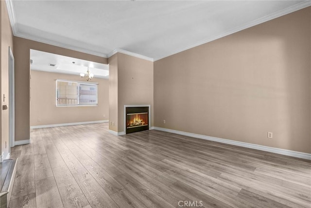 unfurnished living room with wood finished floors, crown molding, baseboards, a chandelier, and a glass covered fireplace