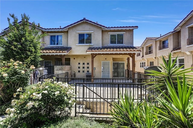 view of front facade with a tiled roof, fence, stucco siding, and central AC
