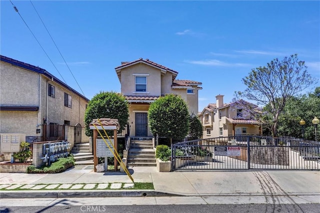 mediterranean / spanish-style house featuring stucco siding, a tile roof, fence, and a gate