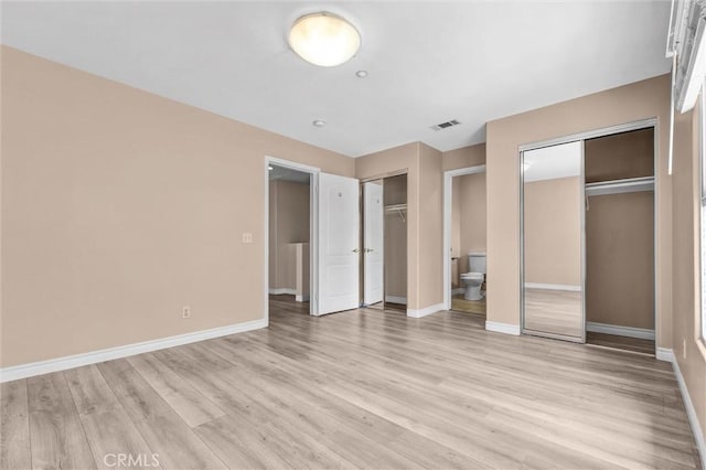 unfurnished bedroom with multiple closets, light wood-style flooring, baseboards, and ensuite bathroom