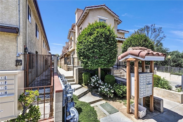 view of property exterior featuring mail area, stucco siding, fence, and a tiled roof
