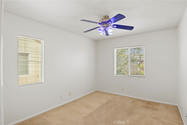 spare room featuring light colored carpet, baseboards, and ceiling fan