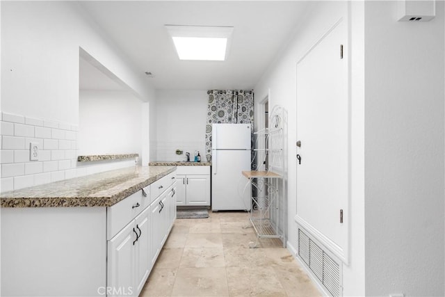 kitchen featuring freestanding refrigerator, white cabinets, and tasteful backsplash