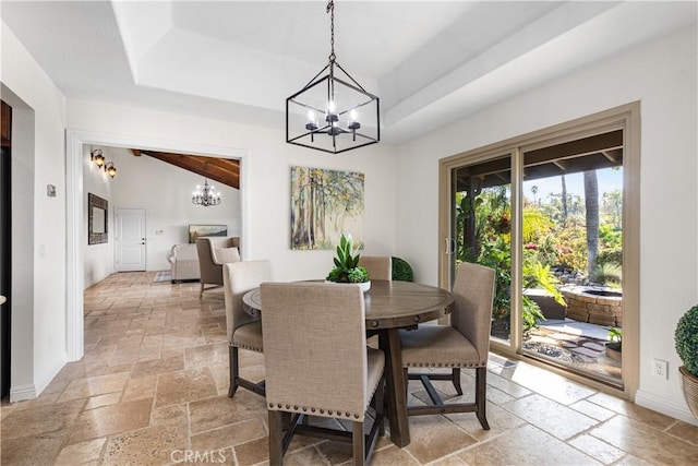 dining room with stone tile floors, a chandelier, vaulted ceiling, and a raised ceiling