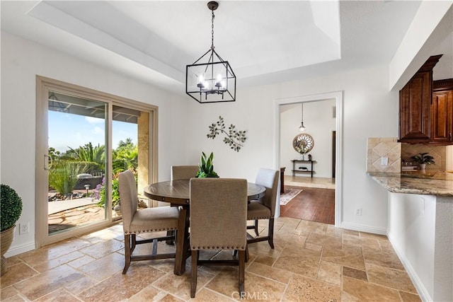 dining room with stone tile flooring, a raised ceiling, a chandelier, and baseboards