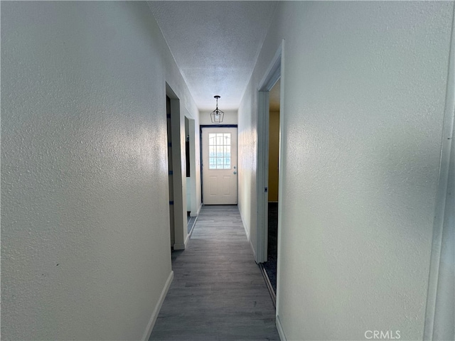hallway featuring baseboards, a textured wall, and wood finished floors