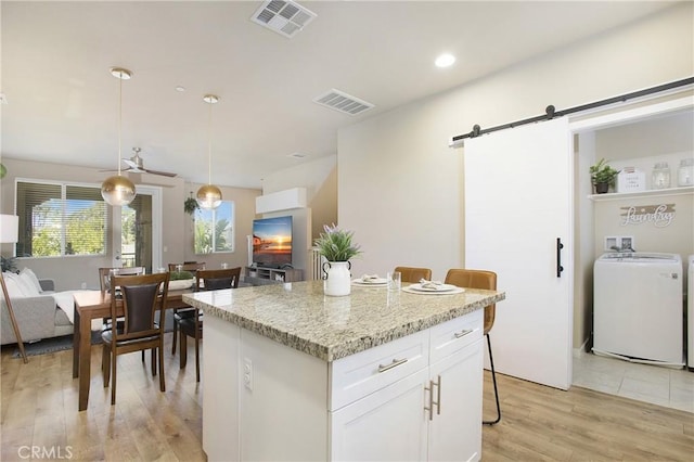 2651 W Lincoln Ave Unit 40, Anaheim, CA 92801 - kitchen with a barn door, light wood-style flooring, a kitchen island, white cabinetry, and hanging light fixtures