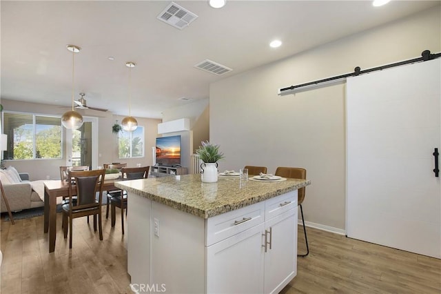 2651 W Lincoln Ave Unit 40, Anaheim, CA 92801 - kitchen featuring a barn door, light wood-type flooring, white cabinets, a center island, and decorative light fixtures