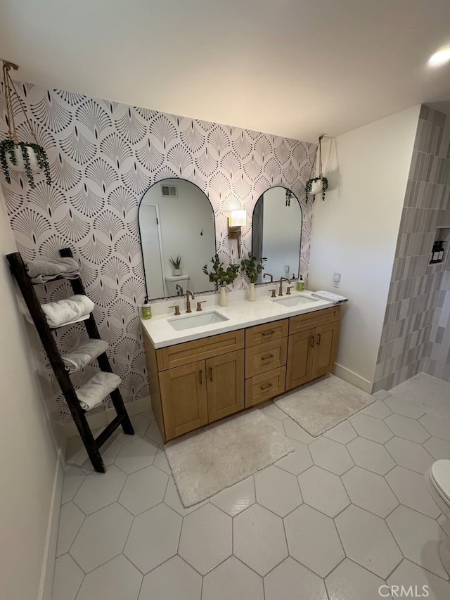 bathroom featuring baseboards, wallpapered walls, double vanity, toilet, and tile patterned floors