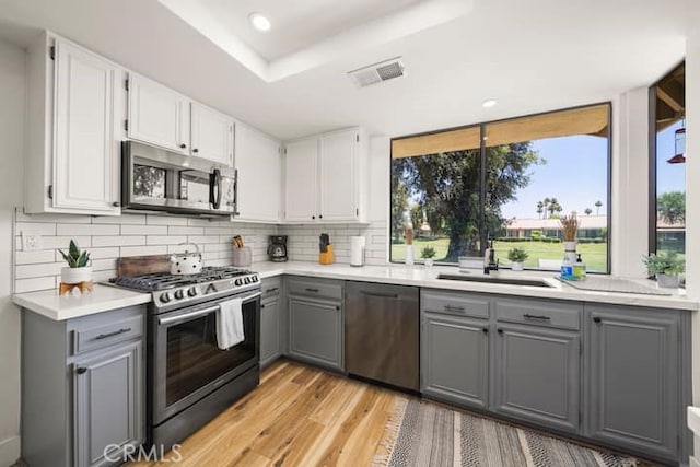 kitchen featuring stainless steel appliances, gray cabinets, a sink, decorative backsplash, and light wood finished floors