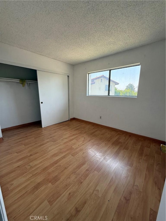 unfurnished bedroom featuring light wood-style flooring, baseboards, a textured ceiling, and a closet