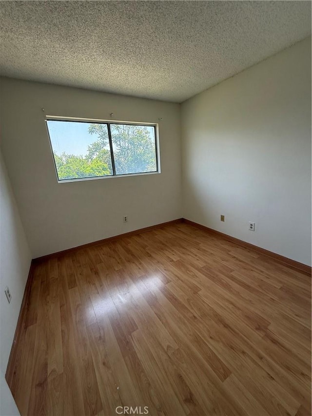 empty room with light wood finished floors, a textured ceiling, and baseboards