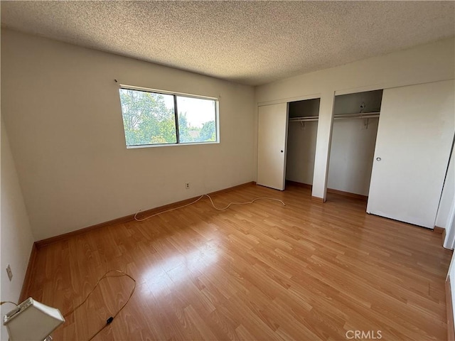 unfurnished bedroom featuring two closets, a textured ceiling, light wood finished floors, and baseboards