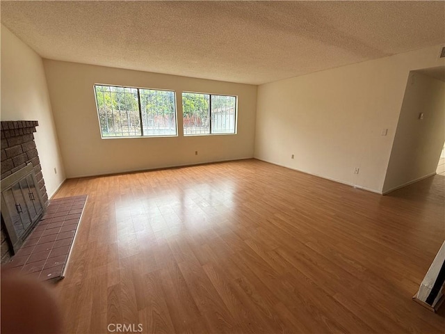 unfurnished living room featuring a fireplace, light wood-type flooring, and a textured ceiling