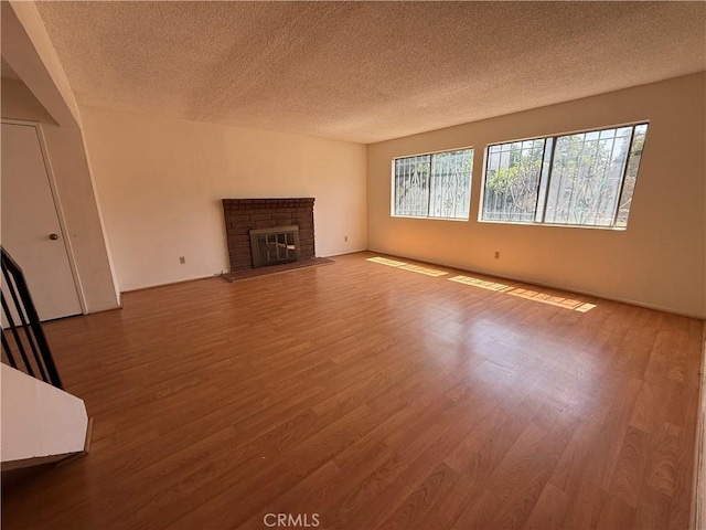 unfurnished living room with a textured ceiling, wood finished floors, and a brick fireplace