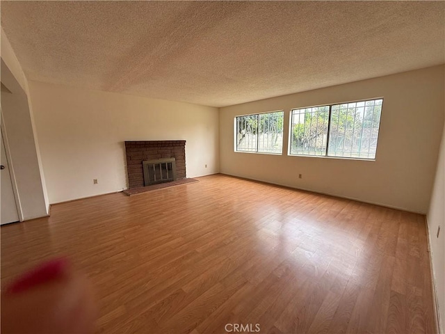 unfurnished living room with light wood finished floors, a textured ceiling, and a fireplace