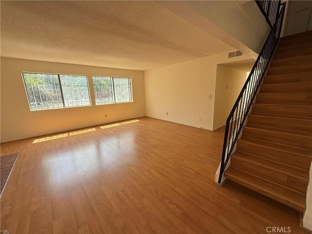 unfurnished room featuring a textured ceiling, wood finished floors, and stairway