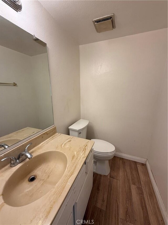 half bath with wood finished floors, toilet, vanity, and baseboards