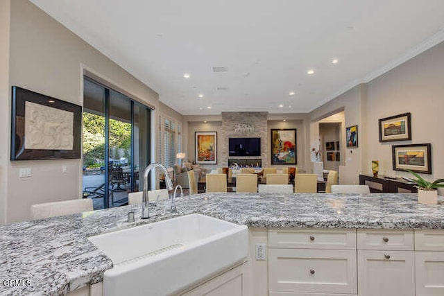 kitchen with a sink, light stone countertops, white cabinets, recessed lighting, and ornamental molding