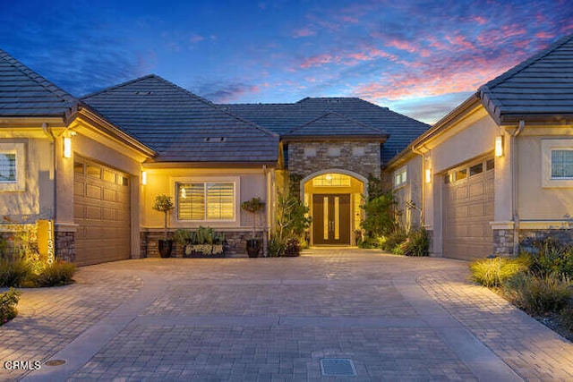 view of front of house featuring a garage, stone siding, decorative driveway, and french doors