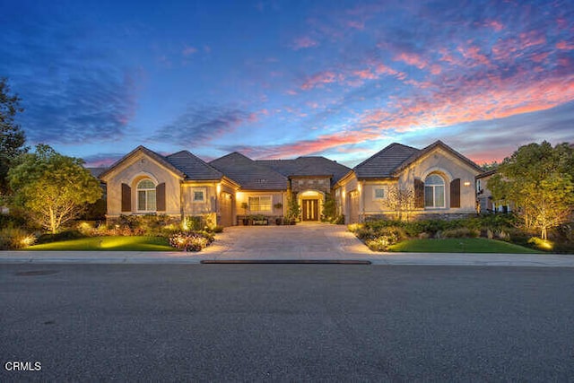 view of front of property featuring stucco siding, stone siding, and curved driveway