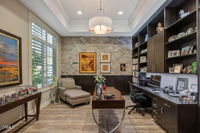 office area with light wood-style floors, a tray ceiling, crown molding, a wainscoted wall, and built in study area