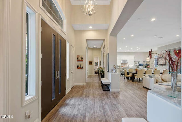 foyer featuring wood finished floors, recessed lighting, a chandelier, a high ceiling, and baseboards