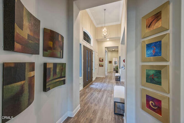 hall featuring ornamental molding, wood finished floors, baseboards, and a towering ceiling