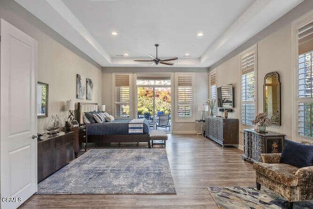 bedroom featuring a raised ceiling, multiple windows, wood finished floors, and recessed lighting