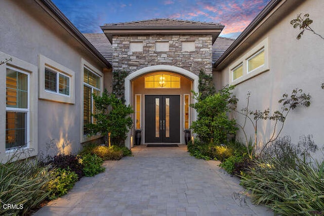 exterior entry at dusk with french doors, stucco siding, and stone siding